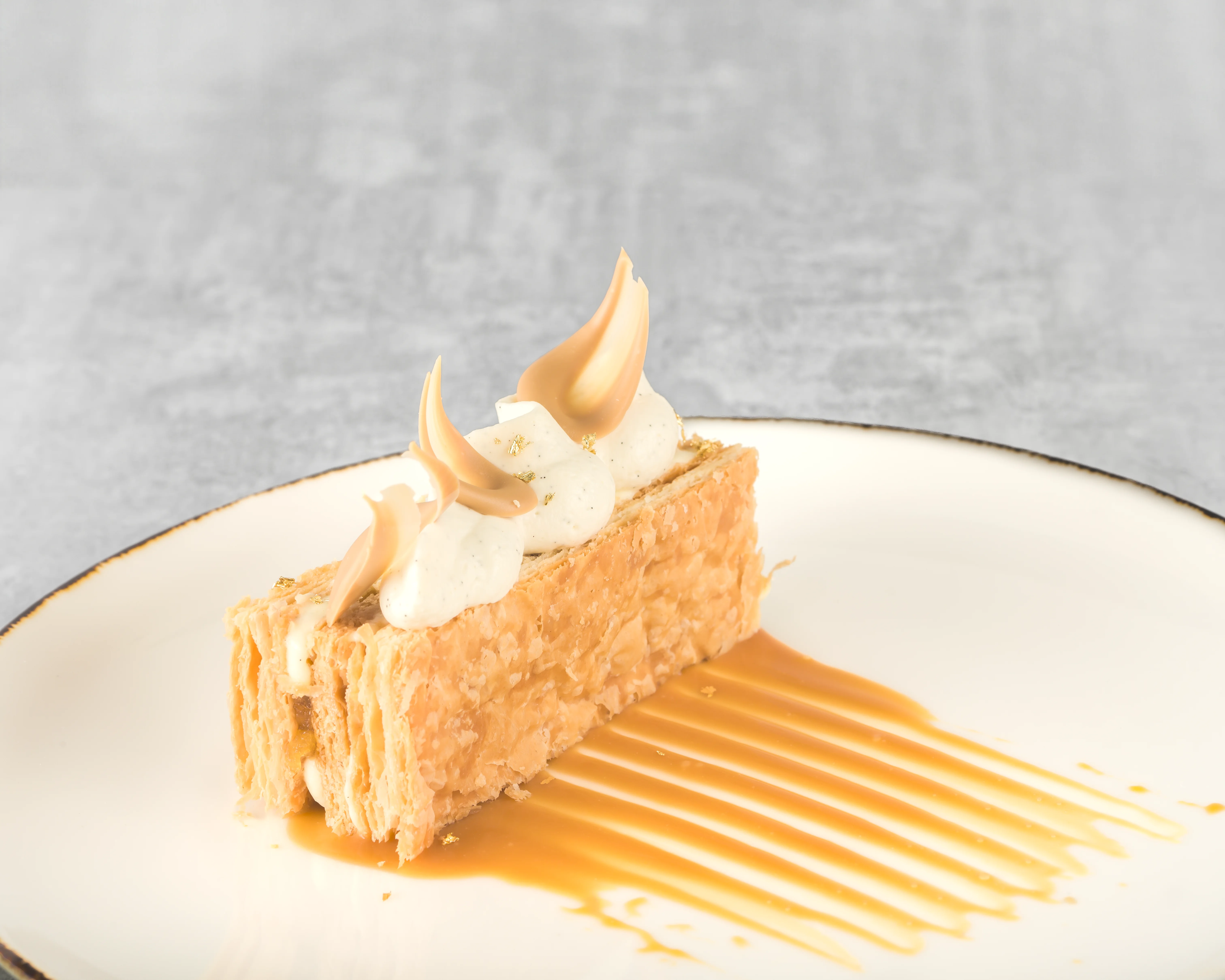 Fine dining mille-feuille with delicate layered puff pastry, piped caramel cream peaks, and a caramel sauce pool on a cream-coloured plate