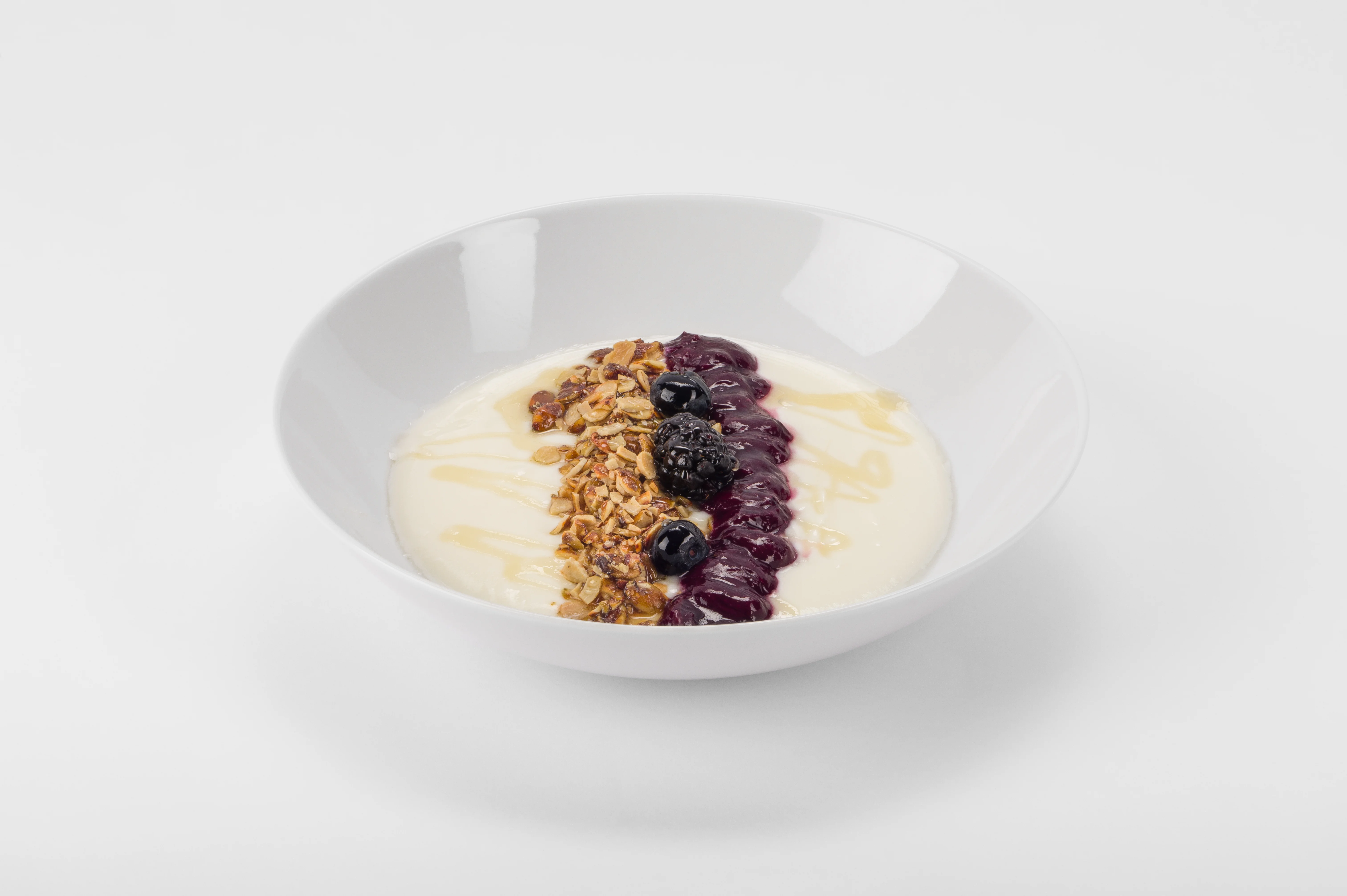 Breakfast bowl with yogurt, granola, dried cranberries, fresh blueberries, and a honey drizzle, styled in a wide white bowl on a white background